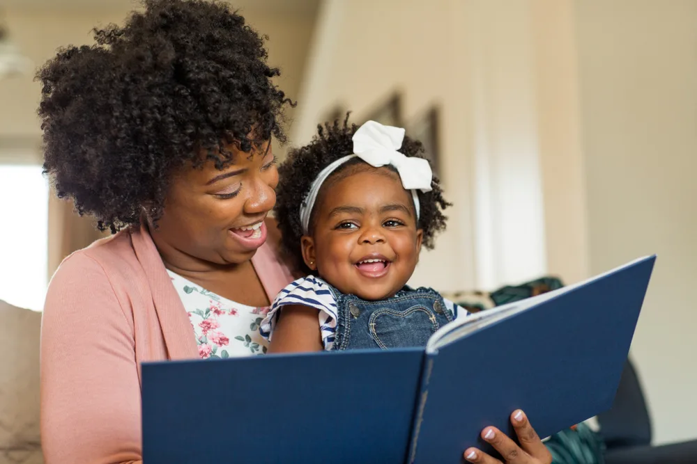 Photo: Mother reading to a smiling toddler who is sitting on her lap.